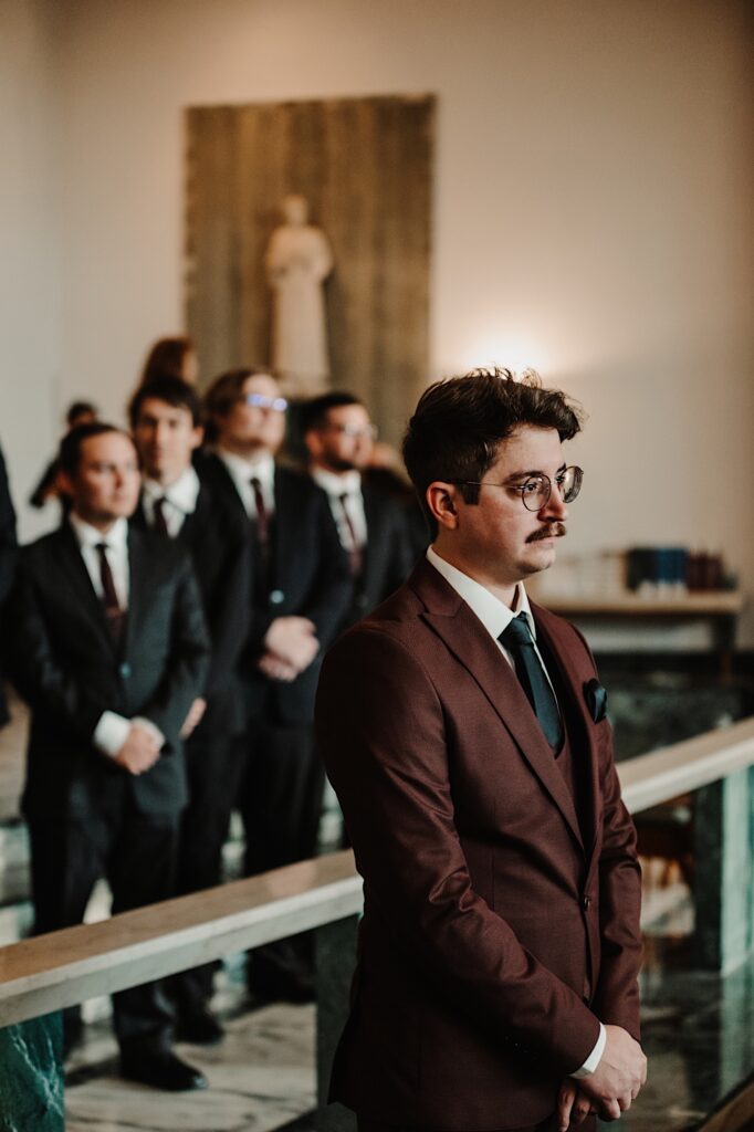 A groom stands in a church with his groomsmen behind him as he waits for his bride to be to walk down the aisle