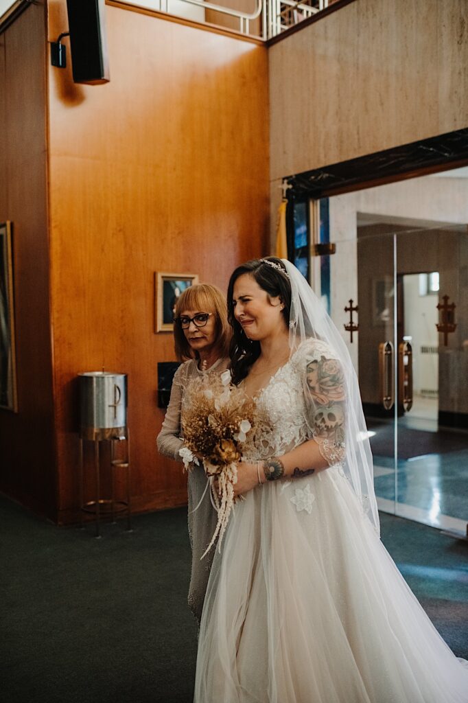 A bride tears up as she enters her wedding ceremony space while being escorted by her mother