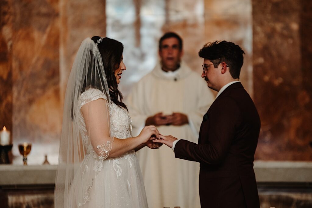 A bride puts a wedding ring on the finger of the groom during their fall wedding ceremony in Chicago