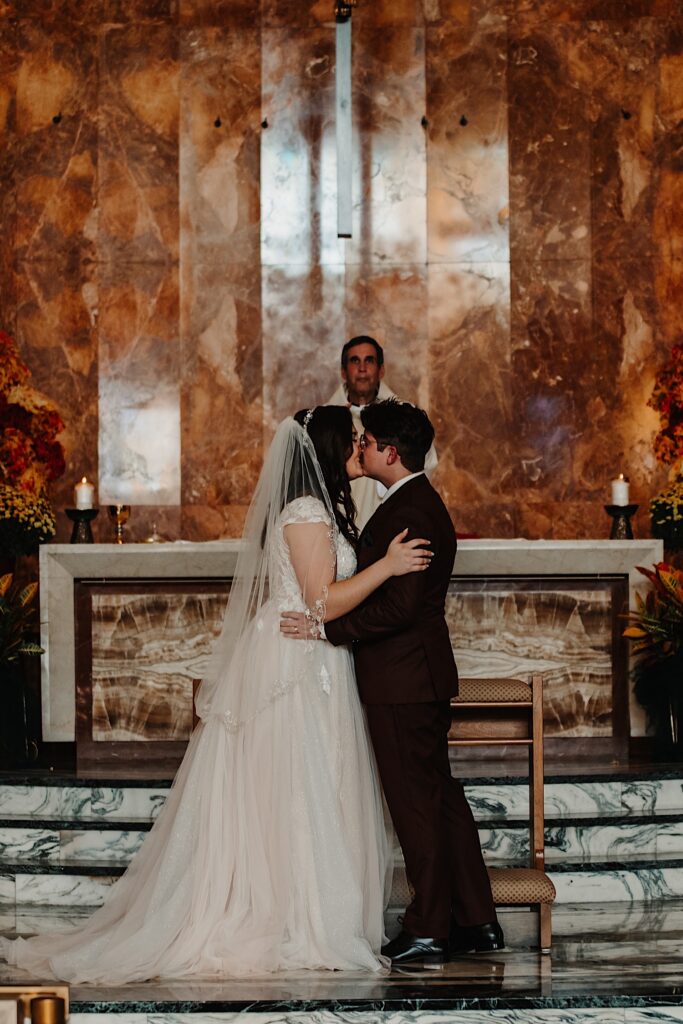 A bride and groom kiss in a church during their wedding ceremony