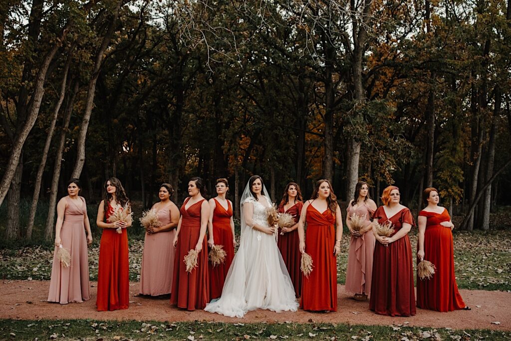 A bride and her bridesmaids on either side of her pose during a fall wedding in Chicago, the trees behind them have all changed color
