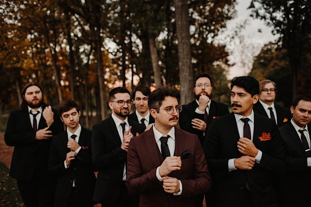 A groom surrounded by his groomsmen all adjust their cuffs and ties while in a park during a fall wedding in Chicago