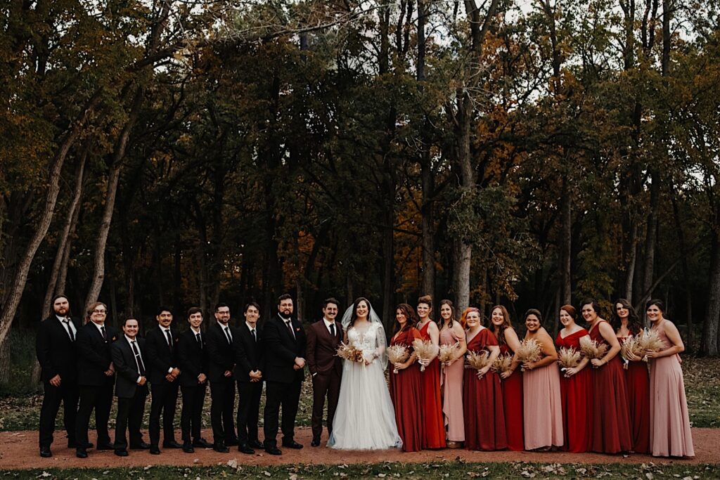 A bride and groom stand in a park in Chicago during their fall wedding, on either side of them are their respective wedding parties