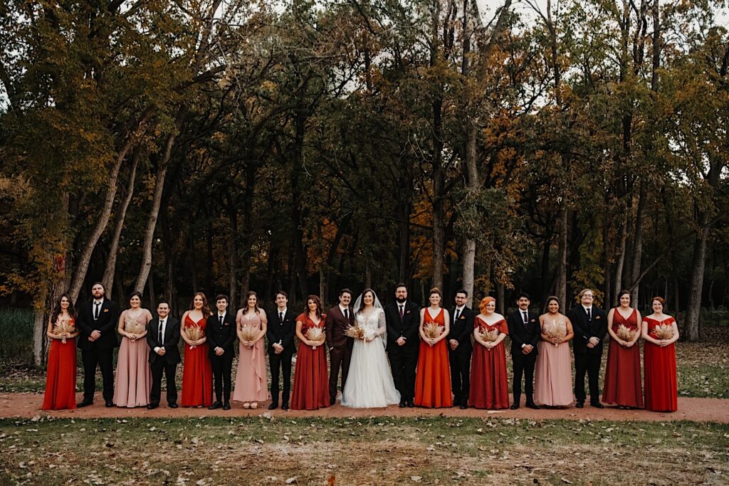 A bride and groom stand with their wedding parties on either side of them in a park in Chicago during their fall wedding