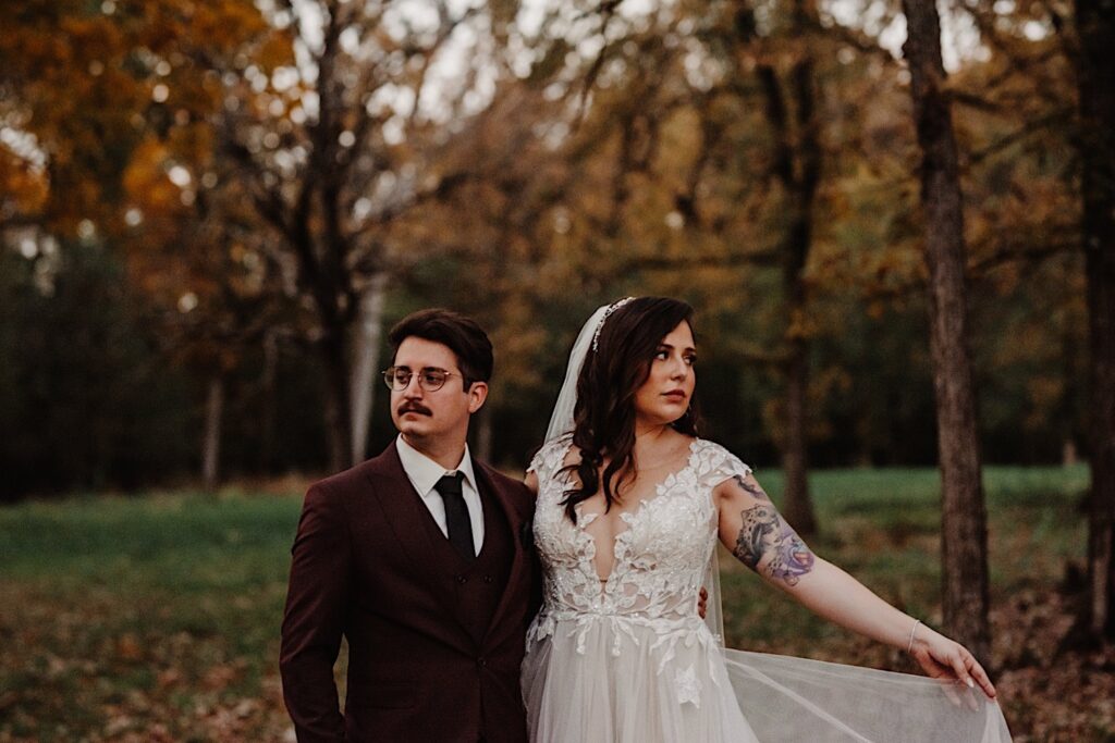 A bride and groom stand side by side and look in opposite directions while standing in a park of Chicago during the fall on their wedding day