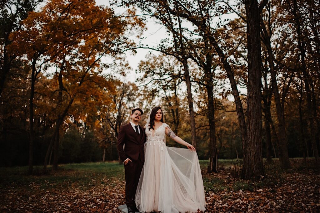 A bride and groom stand side by side and look at the camera while standing in a park of Chicago during the fall on their wedding day