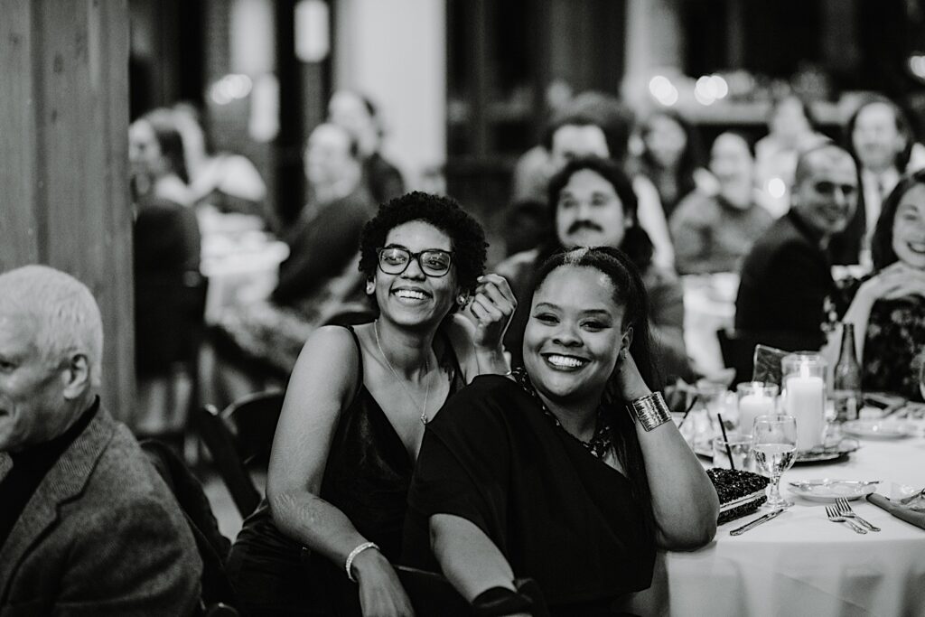 Black and white photo of guests of a wedding reception smiling during speeches