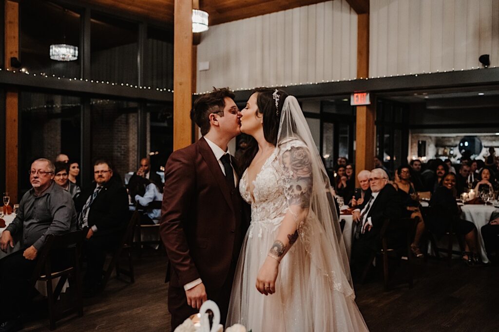 A bride and groom stand and kiss in the middle of the reception space at Oakbrook Bath and Tennis Club during their fall wedding reception in Chicago
