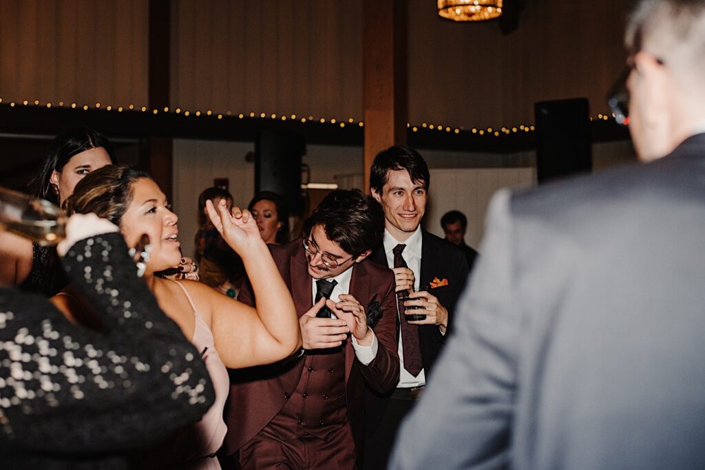A groom claps and celebrates with the guests of his fall wedding in Chicago at their reception space, Oakbrook Bath and Tennis Club