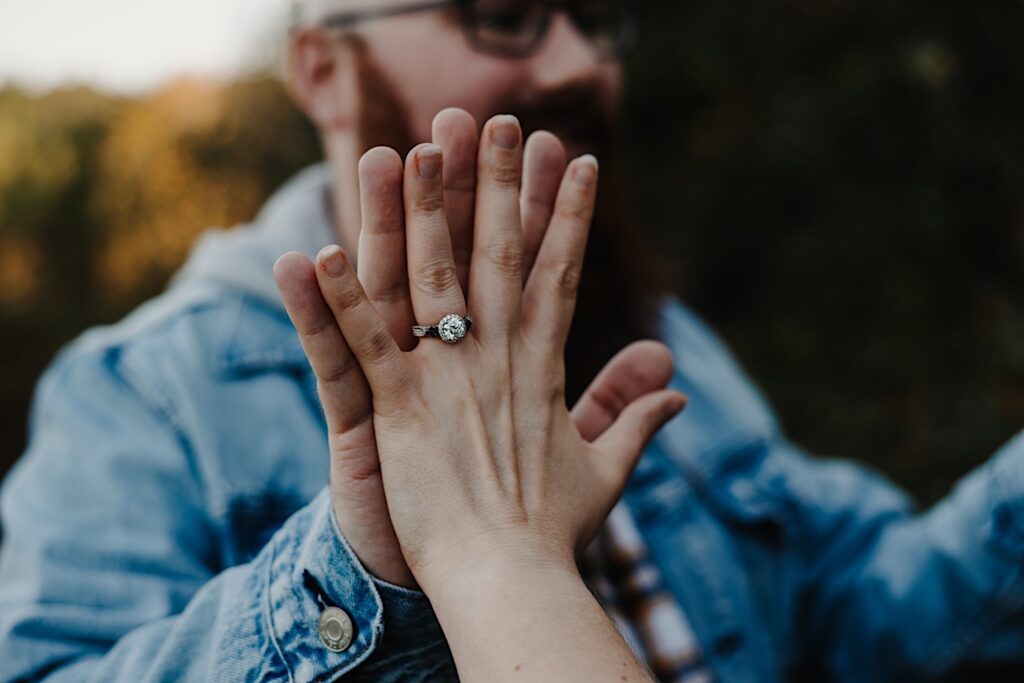 A woman's hand with a ring on it touches a man's hand who is out of focus in the background, photographed by a Chicago engagement photographer