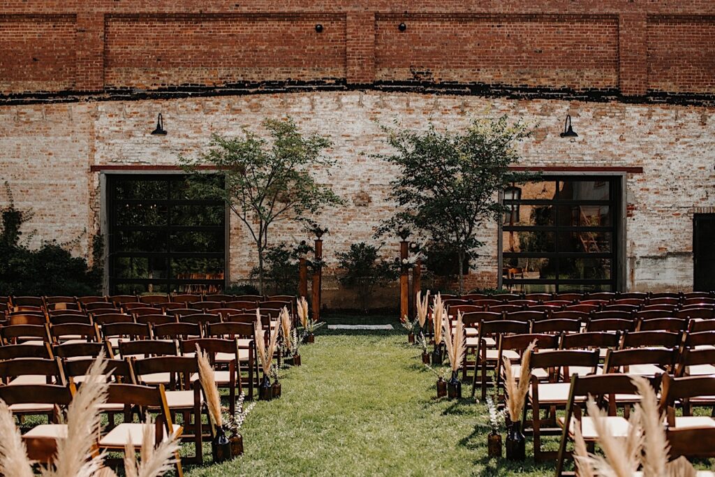 An outdoor ceremony space set up for a wedding with wooden chairs and floral décor in front of a brick wall