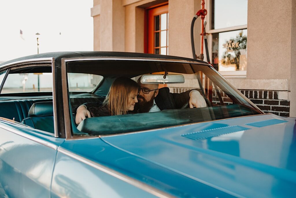 A man puts his arm around a woman and whispers in her ear while they sit inside their classic Chevy SS during their engagement session with a Chicago phtoographer