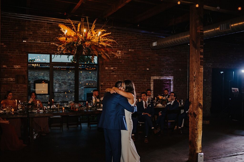 A bride and groom share their first dance of their wedding day as their guests watch in the indoor space of their wedding venue The Cannery in Eureka Illinois