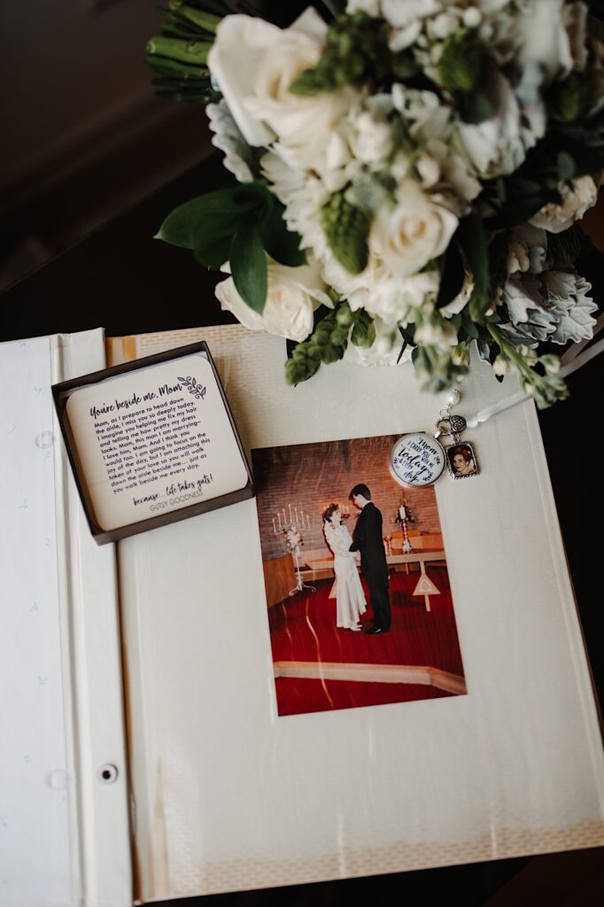 A vintage photo album with a portrait of a wedding couple lays on a table with flowers and a note next to it