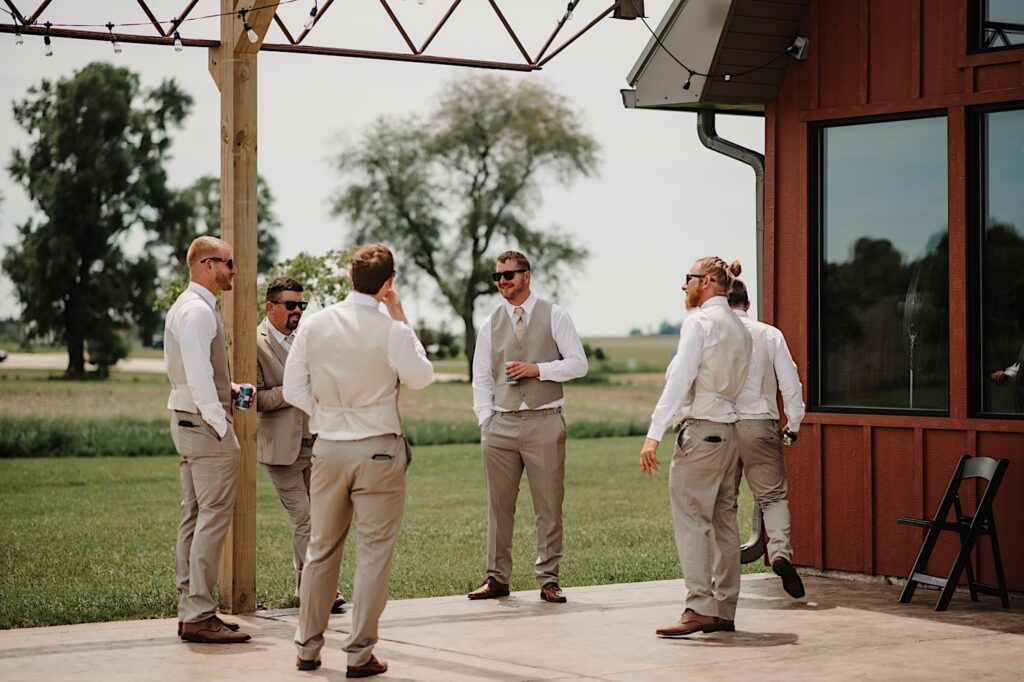 A groom and 5 groomsmen stand outside a house and talk while having a beer before heading to the wedding ceremony, photographed by a Central Illinois wedding photographer