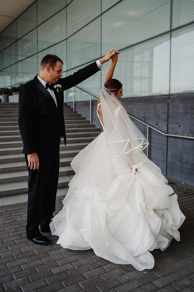 While on an outdoor staircase a bride spins while the groom holds her hand