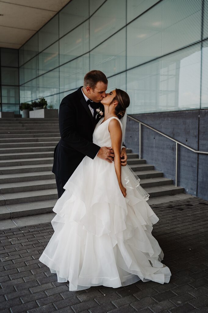 A bride and groom kiss one another while standing on an outdoor staircase