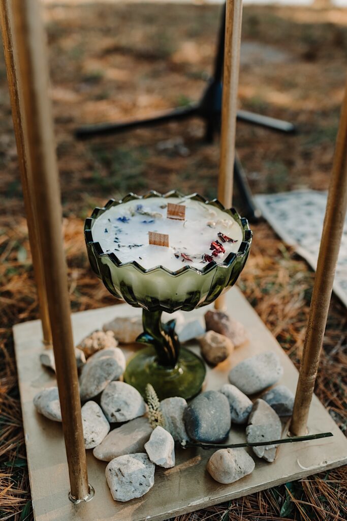 Detail photo of a large glass cup with candle wax in it on the ground surrounded by rocks