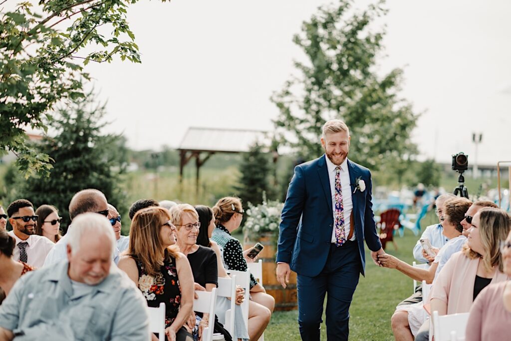 A groom walks down the aisle of his outdoor wedding ceremony at his venue, the Destihl Brewery in Normal, Illinois