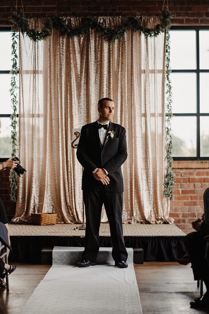 A groom stands in front of a small stage that is decorated for a wedding ceremony