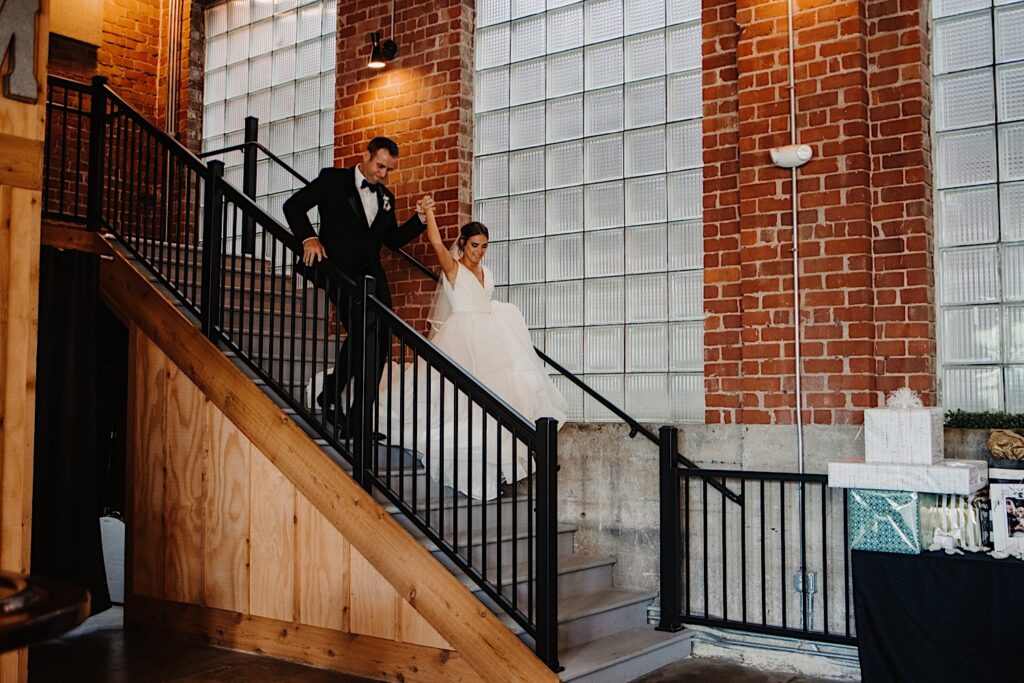 A bride and groom walk down a staircase at Stardust in Davenport to enter the indoor wedding reception space while holding hands and smiling