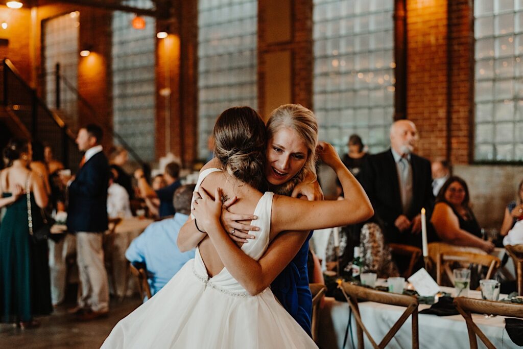 A woman hugs a bride who is facing away from the camera during an indoor wedding reception at Stardust in Davenport