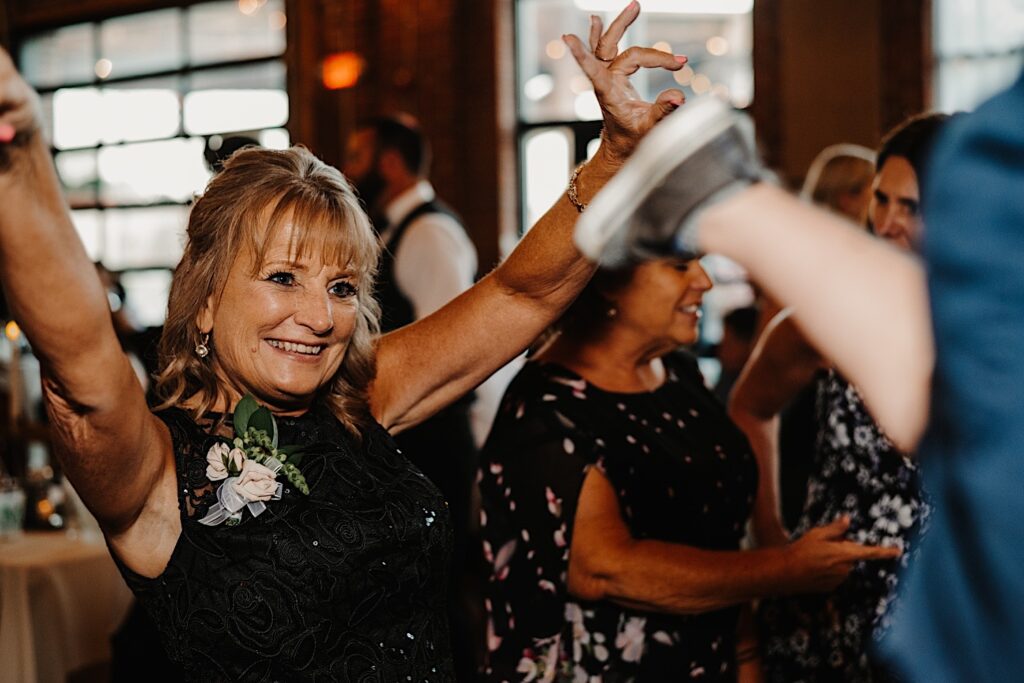 A guest of a wedding smiles while lifting her arms in the air during an indoor wedding reception at Stardust in Davenport