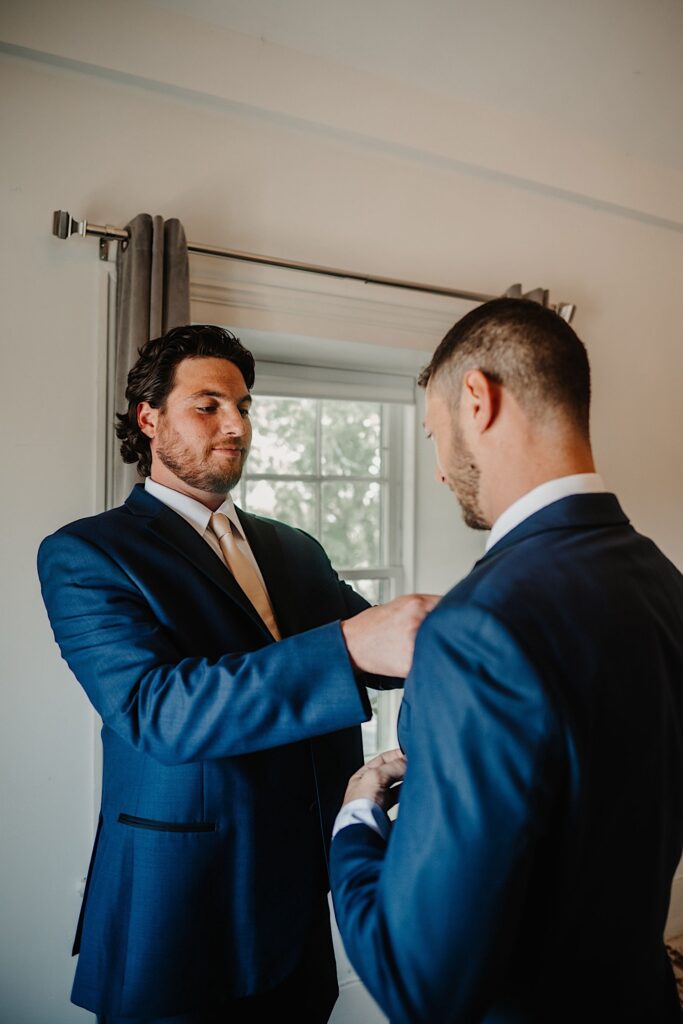 A groomsman helps adjust the grooms tie as they get ready for his wedding day