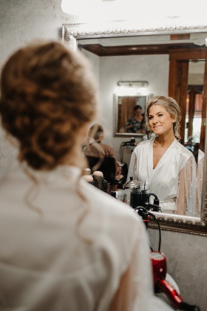 A bride in a mirror smiles as she gets ready for her wedding day