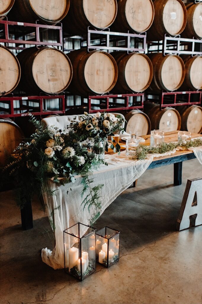 The head table of a wedding decorated with flowers and set up in front of a wall of bourbon barrels