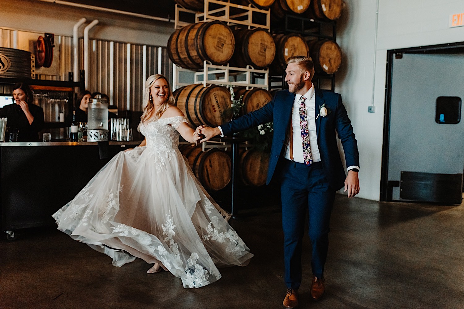 A bride and groom hold hands and smile as they enter their wedding reception at their venue, Destihl Brewery in Normal, Illinois