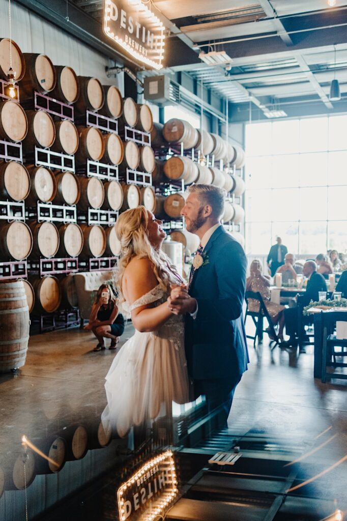 A bride and groom smile as they share their first dance during their indoor wedding reception at Destihl Brewery
