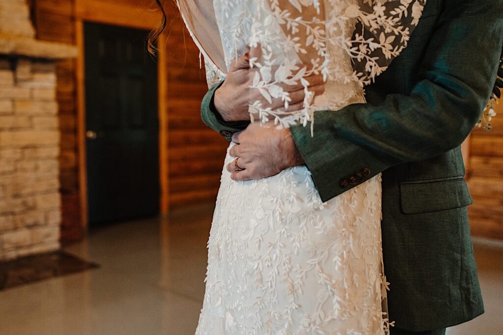 Photo of a bride and groom's torsos as they hug one another inside of a log cabin