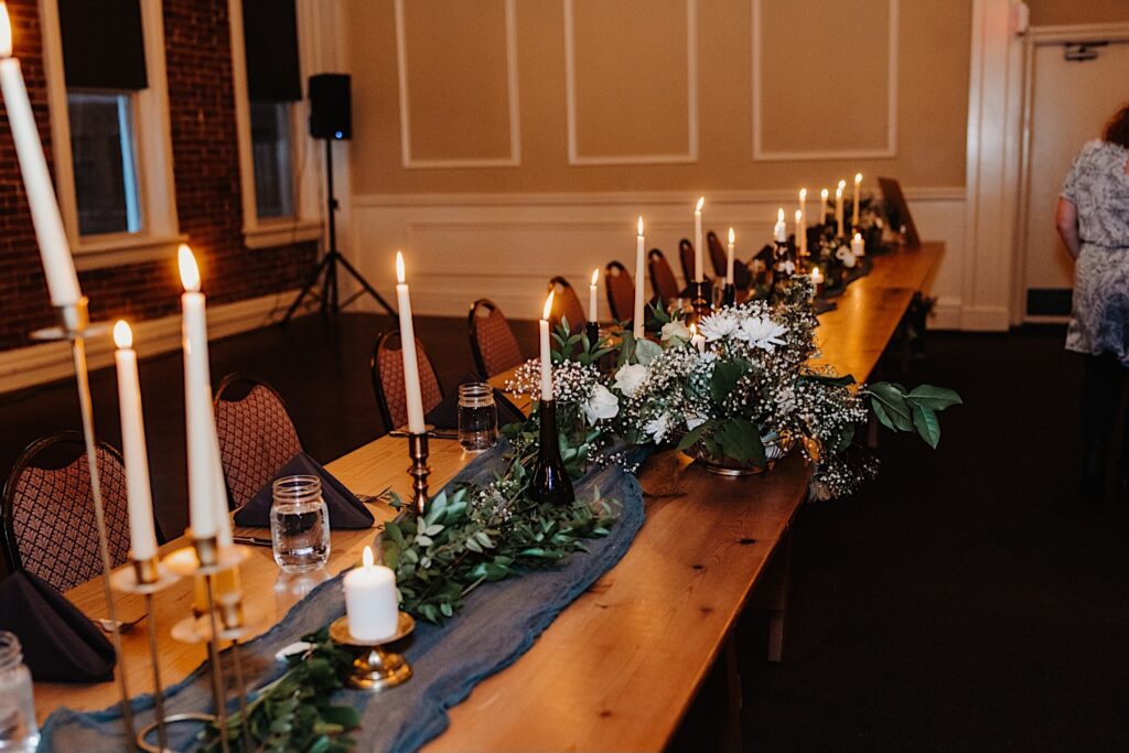 A wood table is decorated with candles, mason jars, and florals for an indoor wedding reception
