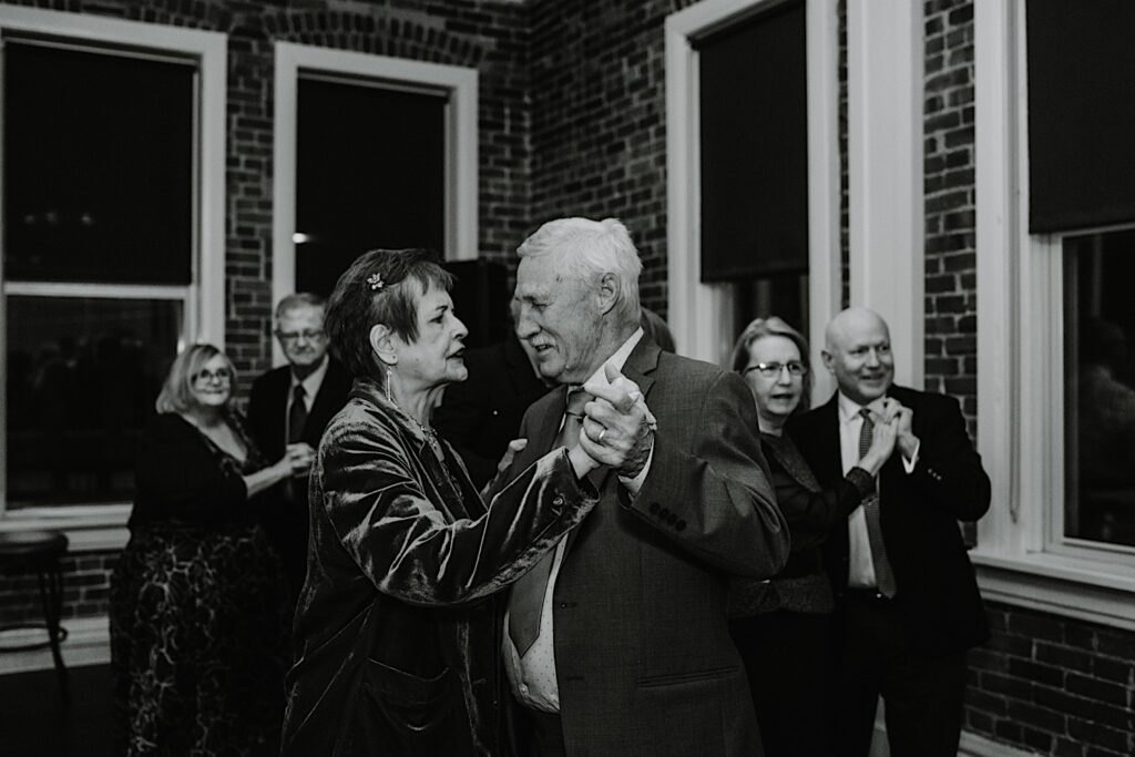 Black and white photo of guests of an intimate fall wedding reception dancing together at the indoor wedding venue in Bloomington Illinois