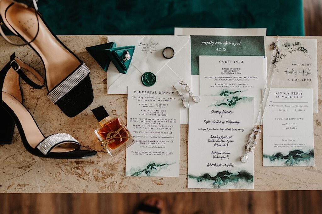 A wedding day flatlay consisting of wedding invites, RSVP's , women's shoes, wedding rings, a necklace, and perfume