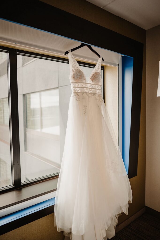 A wedding dress hanging on a hanger in front of a hotel window
