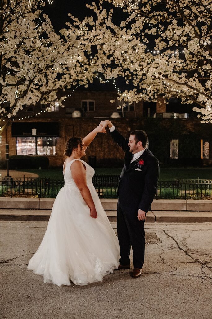 A bride and groom dance with one another while on a street in Chicago under Christmas lights