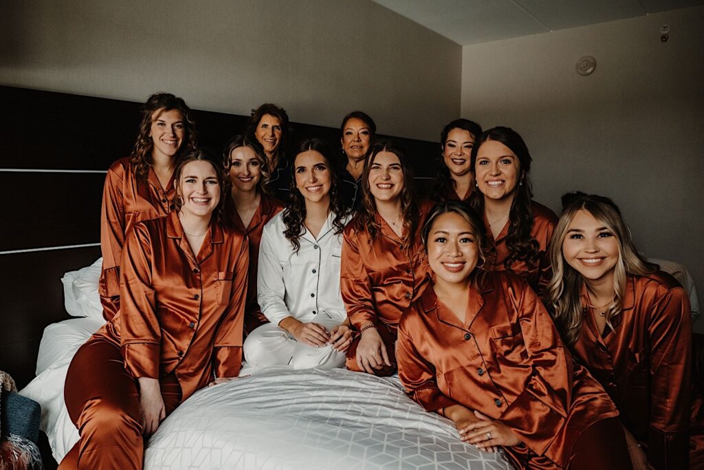 A bride sits on a bed surrounded by her 10 bridesmaids before they get ready for her wedding day