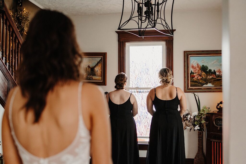 A bride stands in the foreground of the photo with her back to the camera looking at her two bridesmaids who also have their backs to the camera
