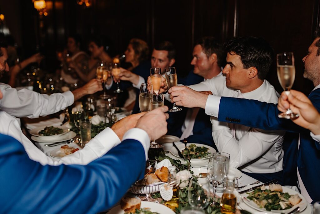 Groomsmen raise their glasses for a toast while seated at a table during a wedding reception