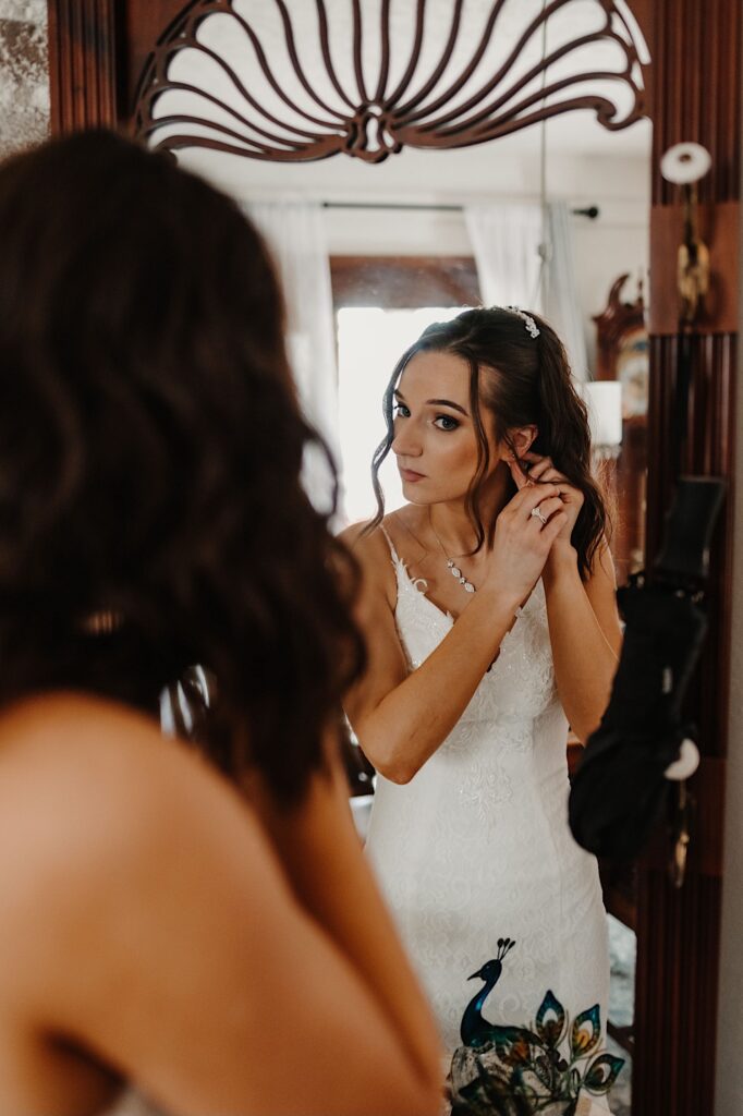 A bride looks in a mirror and adjusts an earring as she gets ready for her wedding day