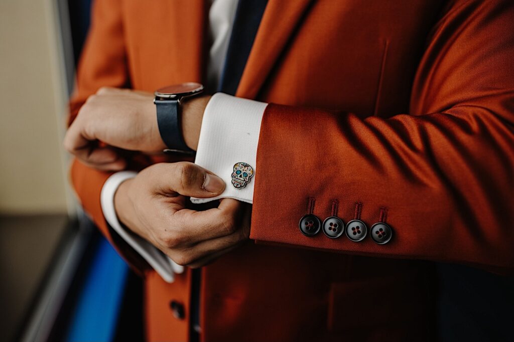 Detail photo of a colorful skull pin as  a cufflink on a man's suit as he adjusts the cuff