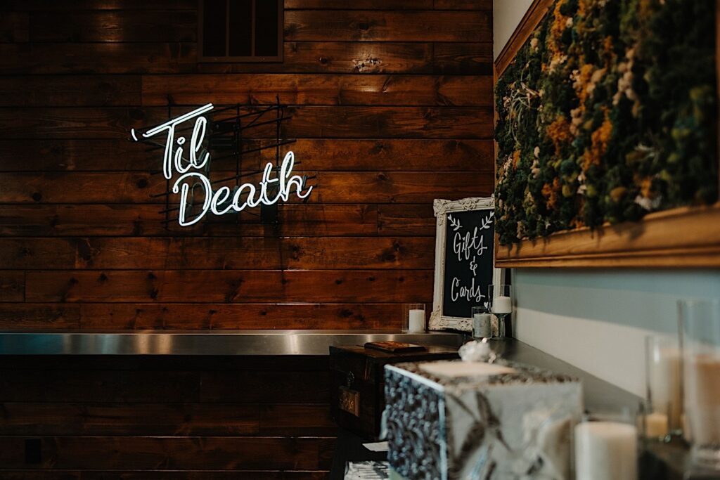 A neon sign on a wooden wall reads "Til Death" and is part of the décor of the wedding venue The Ivy House in Milwaukee