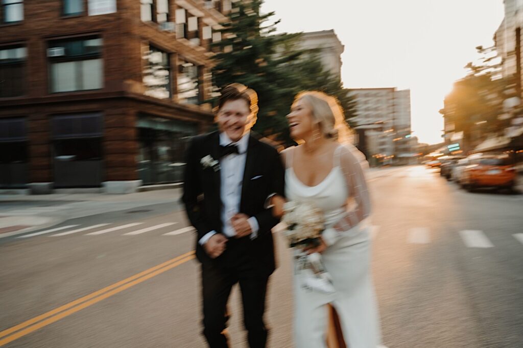 Blurry photo of a bride and groom laughing with one another while running down a street in Chicago with their arms locked together