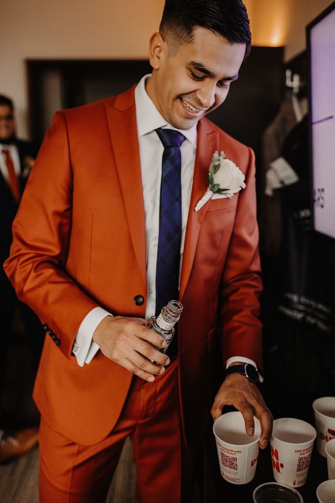 A groom smiles as he is about to pour some liquor into paper Dunkin Donuts cups