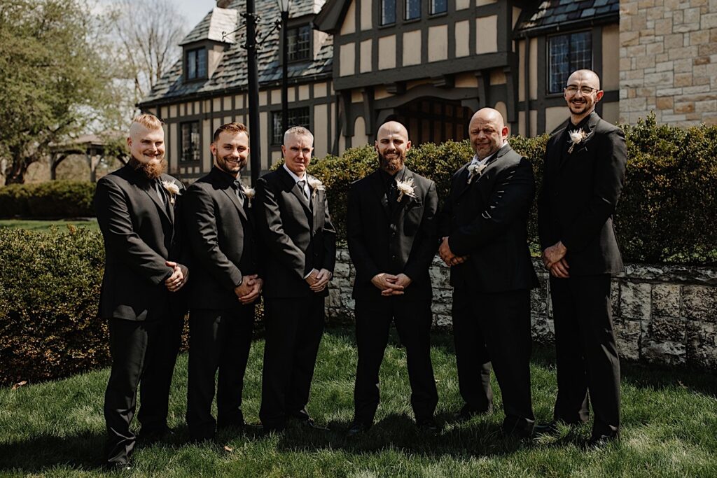 A groom stands in the middle of a group of 5 men consisting of his father, his soon to be father in law, and his three groomsmen