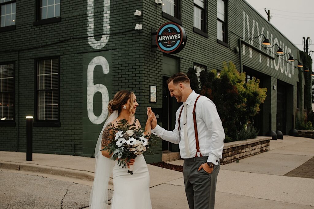 Outside of the front of their wedding venue The Ivy House in Milwaukee, a bride and groom smile at one another while touching their hands together
