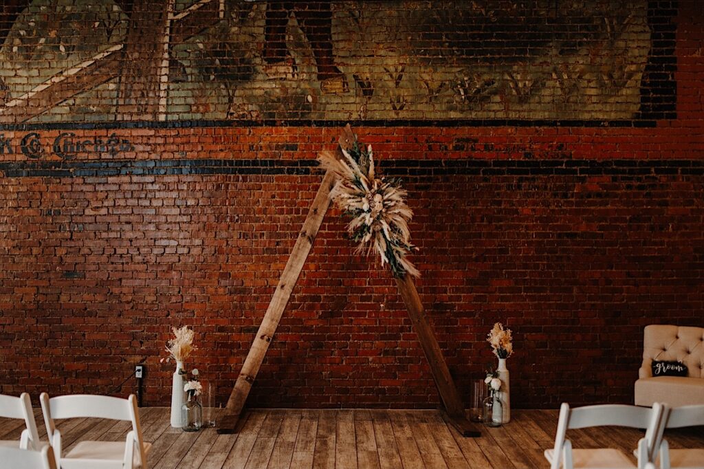 The interior of Reality on Monroe decorated for a wedding, in front of the brick wall is a wooden triangle center piece decorated with flowers and with vases on either side of it