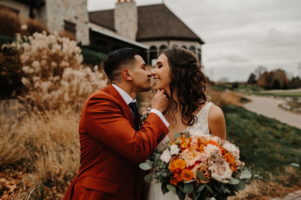 A bride and groom are about to kiss one another while standing outside their wedding venue Mistwood Golf Club in the fall
